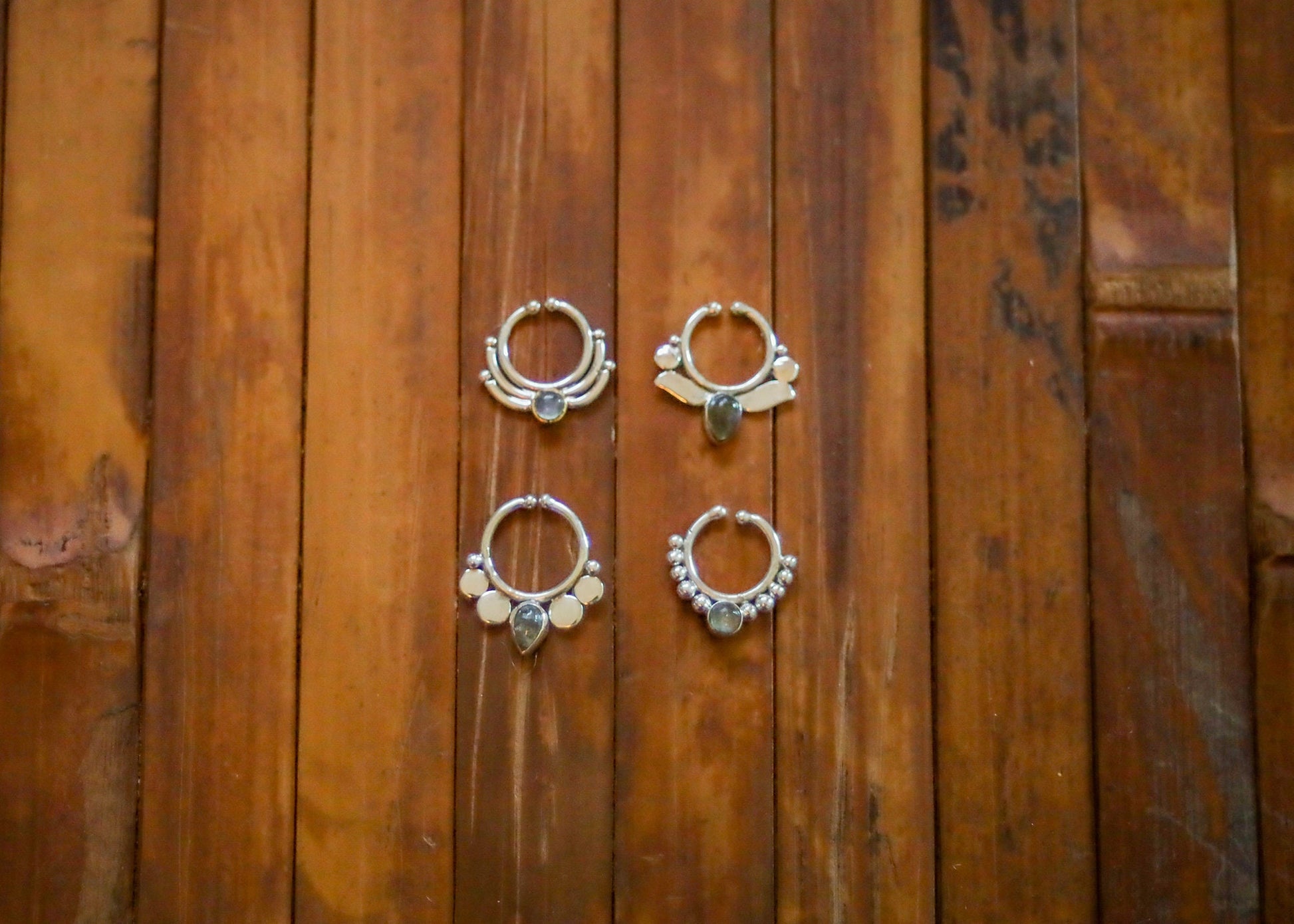 May include: Four silver nose rings with different designs and dark gray gemstones. Each ring has a circular shape with a decorative design and a single gemstone in the center.